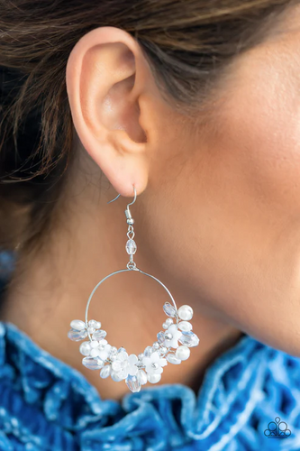 A timeless collection of iridescent crystal-like accents, dainty white pearls, and white floral frames delicately cluster along the bottom of a silver hoop, creating a glamorous glow. The earring attaches to a standard fishhook fitting.  Sold as one pair of earrings.