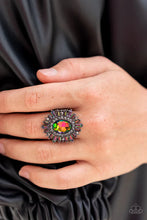 Load image into Gallery viewer, A large oil spill rhinestone sparkles inside a ring of dainty hematite rhinestones. Emerald-cut oil spill and hematite rhinestones fan out from the dazzling center, exploding into a stellar centerpiece atop the finger. Features a stretchy band for a flexible fit. Due to its prismatic palette, color may vary.  Sold as one individual ring.
