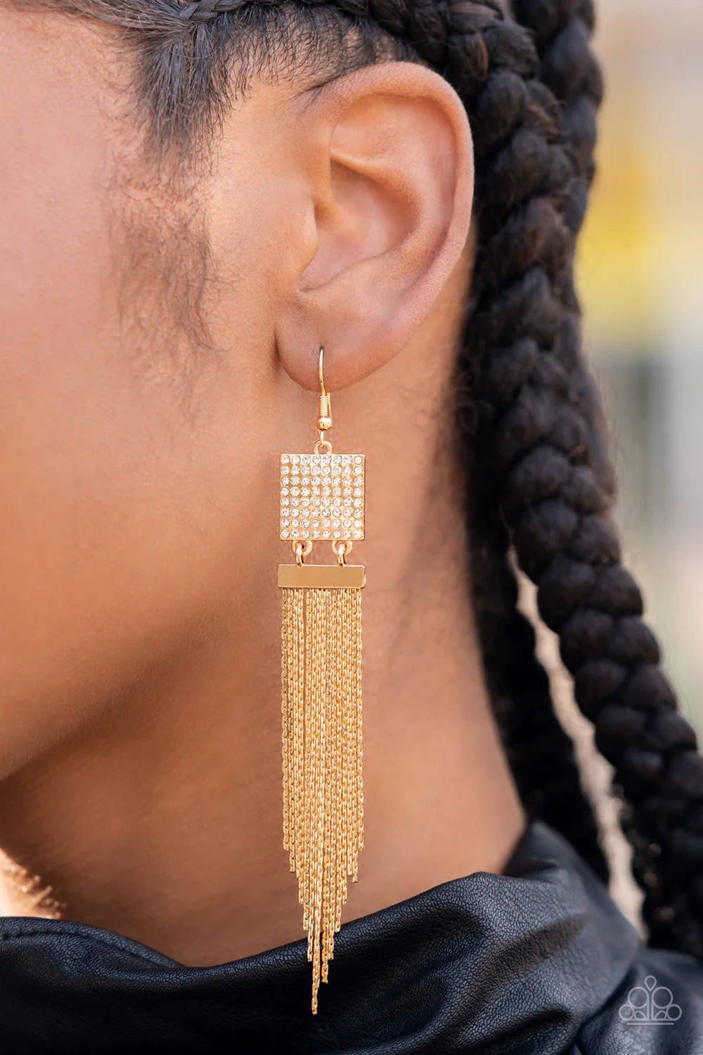 A tapered curtain of flat gold chains cascades from a gold rectangular fitting that delicately links to a gold square frame dotted with dainty white rhinestones, resulting in a trendy tassel. The earring attaches to a standard fishhook fitting. Sold as one pair of earrings.