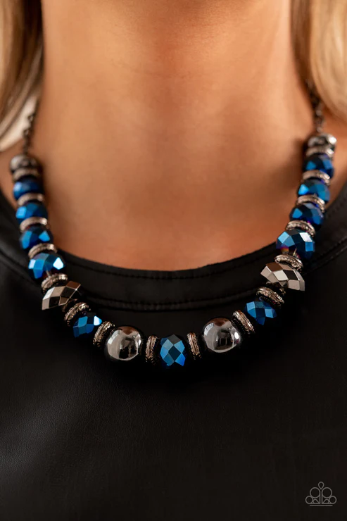 A dramatic assortment of oversized gunmetal beads, textured gunmetal rings, and faceted metallic blue gems delicately glides along an invisible wire below the collar, resulting in a stellar sparkle. Features an adjustable clasp closure.  Sold as one individual necklace. Includes one pair of matching earrings.