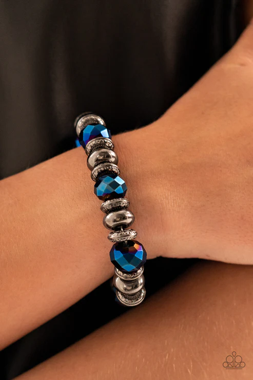 An oversized assortment of textured gunmetal rings, smooth gunmetal beads, and metallic blue crystal-like beads are threaded along stretchy bands around the wrist for a glitzy finish.  Sold as one individual bracelet.