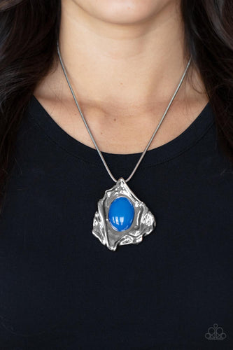A glassy blue oval bead is pressed into the center of an abstract silver frame below the collar, creating a colorful artisan inspired pendant at the bottom of a rounded silver snake chain. Features an adjustable clasp closure.  Sold as one individual necklace. Includes one pair of matching earrings.