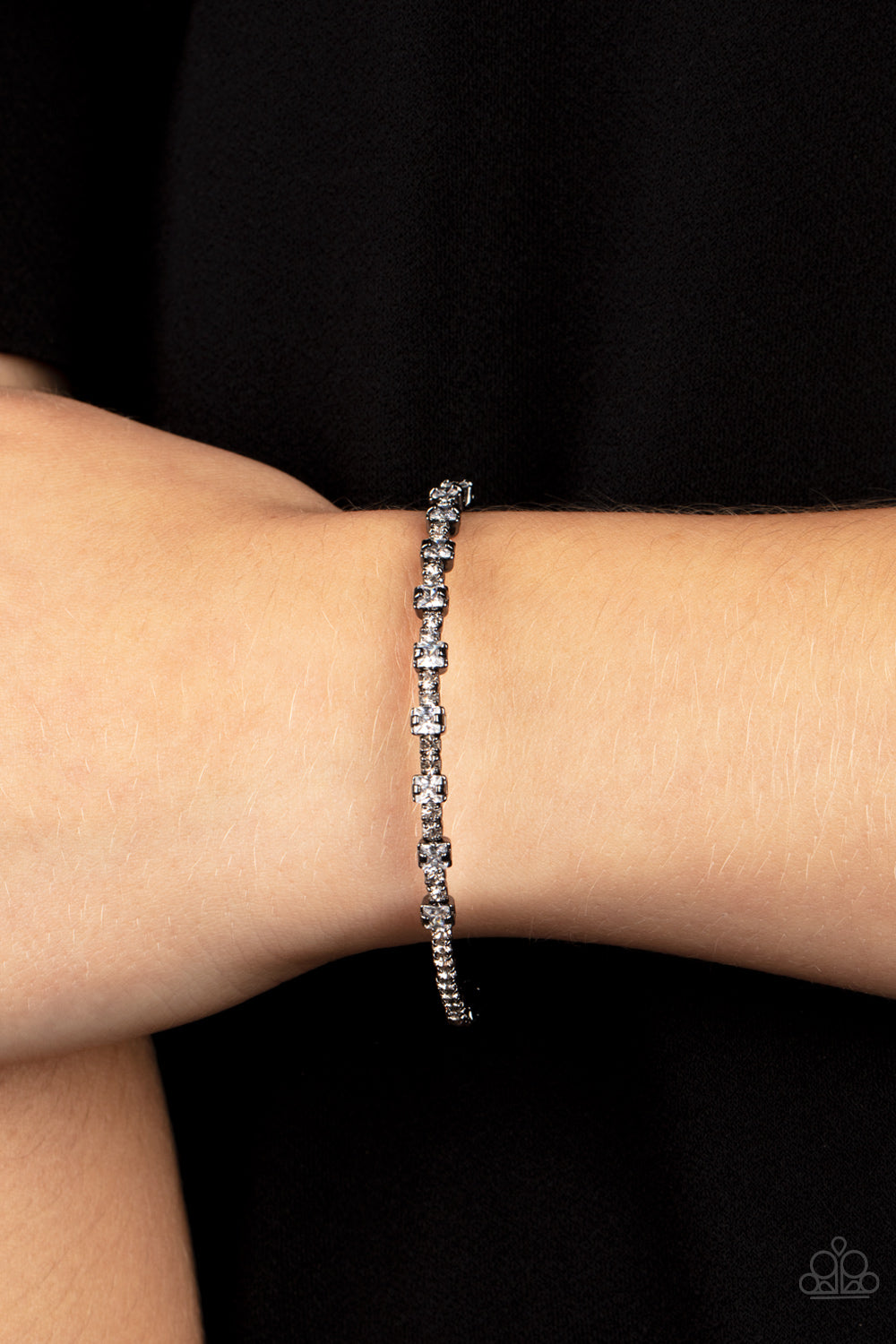 Featuring sleek gunmetal fittings, a classic band of dainty white rhinestones is interrupted with square cut white rhinestones, adding a timeless twist to the stackable cuff.  Sold as one individual bracelet.