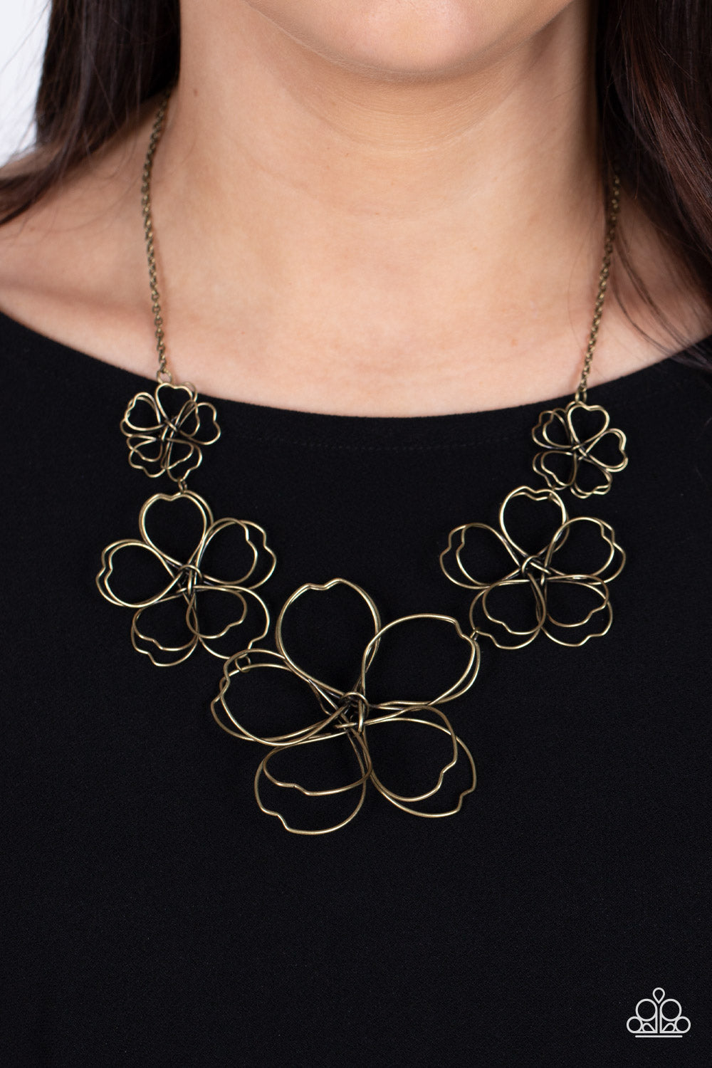 Rustic brass wire delicately twists into oversized blossoms. Gradually increasing in size, the 3D frames elegantly pop beneath the collar. Features an adjustable clasp closure.  Sold as one individual necklace. Includes one pair of matching earrings.