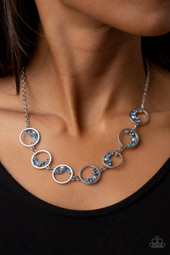 A dainty series of shiny silver rings are sporadically dotted in bubbly rows of glassy and iridescent blue rhinestones as they delicately link below the collar, resulting in an effervescent display. Features an adjustable clasp closure.  Sold as one individual necklace. Includes one pair of matching earrings.