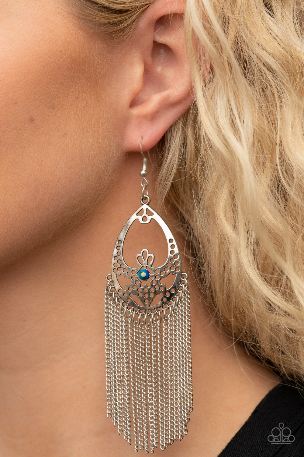 An antiqued curtain of silver chains streams from the bottom of an airy stenciled silver oval frame. An iridescent blue rhinestone adorns the center of the whimsical frame, adding a mystical pop of color to the enchanting fringe. Earring attaches to a standard fishhook fitting.  Sold as one pair of earrings.