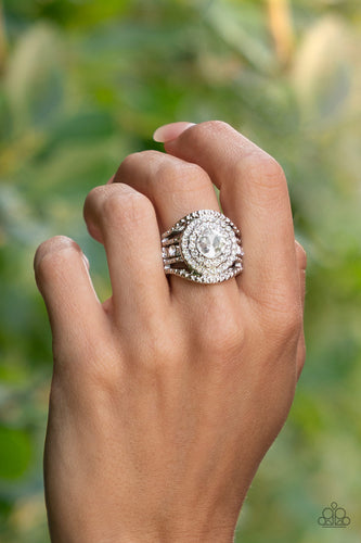Bordered in stacked rings of glassy white rhinestones, a brilliant white gem sits atop layers of silver studded bars that swoop and stack into blinding bands across the finger. Features a stretchy band for a flexible fit.  Sold as one individual ring.