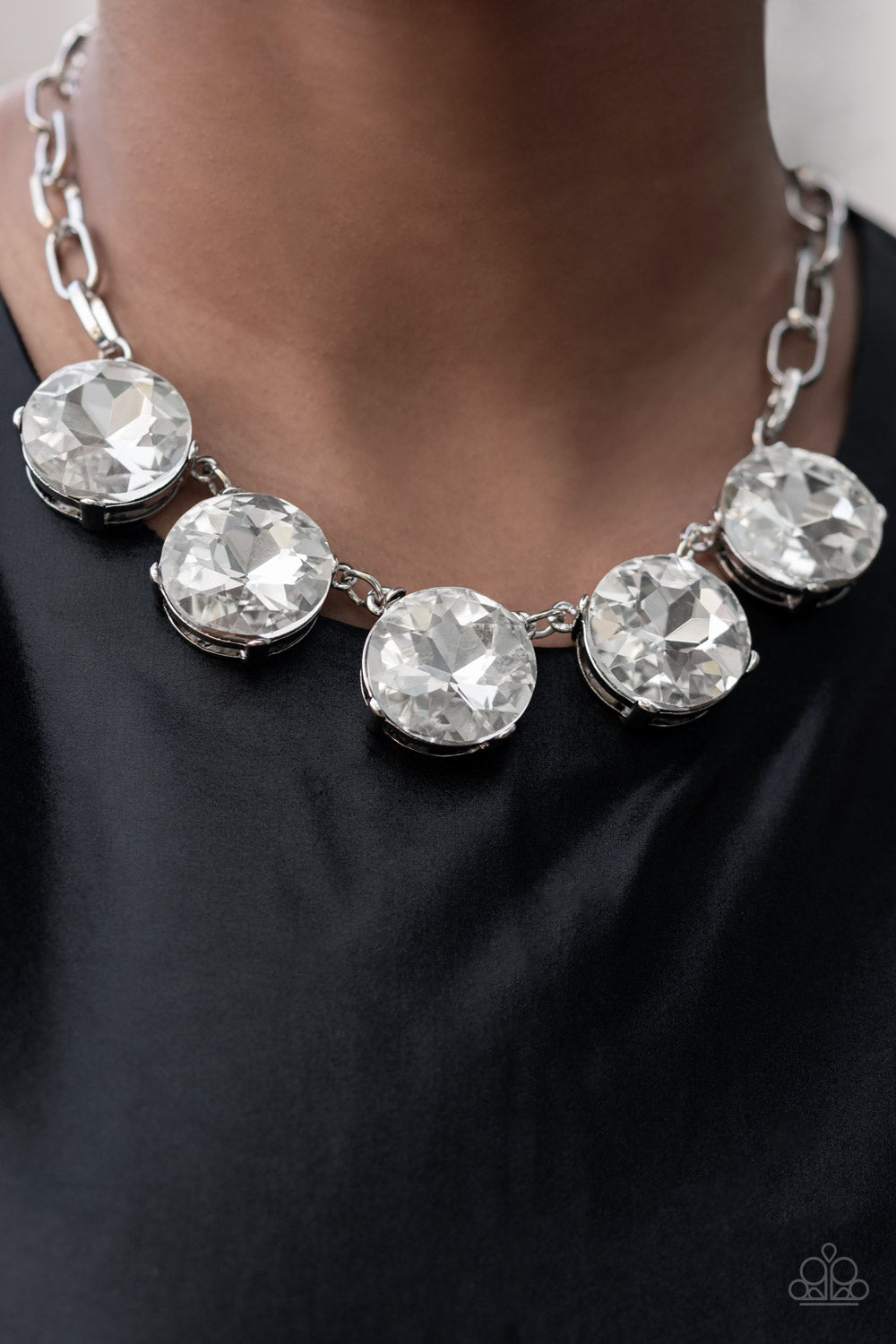 Set in silver pronged fittings, five dramatically oversized brilliant white rhinestones connect across the collar and attach to an oversized silver chain creating a stunning spot-light loving statement piece. Features an adjustable clasp closure.  Sold as one individual necklace. Includes one pair of matching earrings.