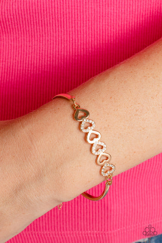 Gold, heart-shaped silhouettes are tilted on their sides, falling in line with variations of the same gold frames encrusted in white rhinestones. The alternating pattern of metallic sheen and glittery shimmer adds eye-catching detail, as the hearts connect into a curved pendant that curls around the wrist. Features an adjustable clasp closure.  Sold as one individual bracelet.
