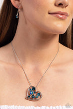 Load image into Gallery viewer, Cascading from a silver snake chain, a thick, sideways sliding-heart silhouette falls down the neckline for a romantic statement. Haphazardly scattered across the inside of the heart frame, a glittery collection of blue and iridescent blue round rhinestones in varying sizes shimmer and shine for a refined finish. Features an adjustable clasp closure. Due to its prismatic palette, color may vary.  Sold as one individual necklace. Includes one pair of matching earrings.
