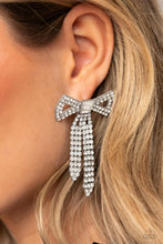Load image into Gallery viewer, Featuring silver square fittings, high-sheen bands of silver, adorned in sparkling white rhinestones loop into a stunning bow charm, creating a classy statement at the ear. Featured in the center of the classy design, a trio of emerald-cut white gems tie the bow together emitting further sheen and glitz. Earring attaches to a standard post fitting.  Sold as one pair of post earrings.
