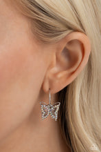 Load image into Gallery viewer, A small, skinny, shiny silver hoop curves around the ear in a timeless fashion. A shiny silver ball is affixed to the end of the hoop, reminiscent of a barbell fitting. An iridescent rhinestone-encrusted butterfly frame, layered in front of a shiny silver airy butterfly frame, slides along the curvature of the hoop, adding a whimsical hint of shimmery movement. Earring attaches to a standard post-fitting. Hoop measures approximately 1/2&quot; in diameter. Due to its prismatic palette, color may vary.
